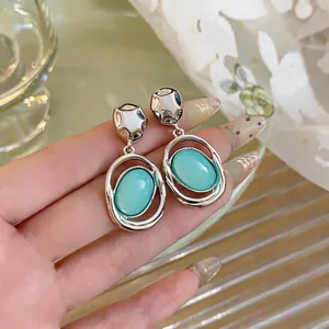 Close-up of silver-tone oval drop earrings featuring a smooth turquoise cabochon stone inlay