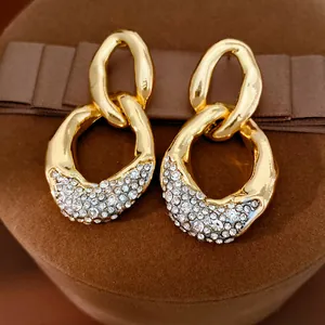 Nahaufnahme von goldfarbenen, klobigen Ohrringen mit glitzernden weißen Strasssteinen.