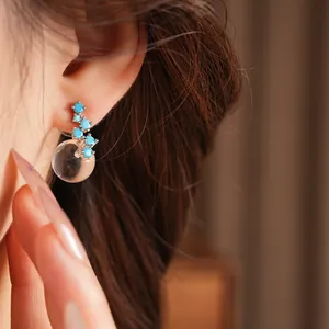 Close-up of elegant earrings with blue stones and clear resin bead on model