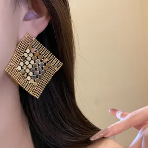 Close-up detail of oversized gold geometric sequin mesh tassel earrings on model