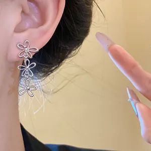 Close-up detail of a silver hollow flower tassel clip-on earring worn on the ear.