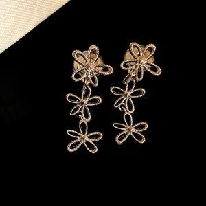Close-up of golden hollow flower tassel clip-on earrings with textured metal finish
