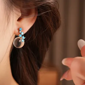 Detailed macro view of elegant blue zircon stud earrings with clear resin sphere on ear