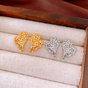 Close-up detail of textured heart-shaped zircon stud earrings in gold and silver plating