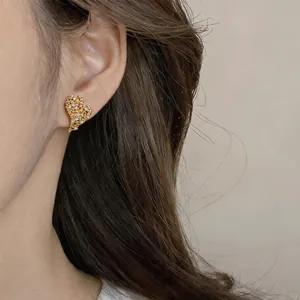 Close-up detail of elegant 18k gold plated heart-shaped zircon earrings worn on ear