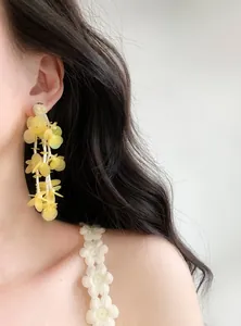 Detailed view of handmade yellow glass bead floral tassel earrings worn on a model.