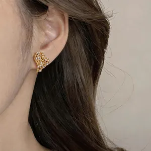Detailed close-up view of a gold-plated heart stud earring with zircons worn on model ear