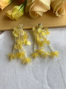 Close-up of yellow glass bead and sequin petal tassel earrings on white linen fabric