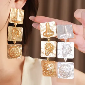 Macro detail of surrealist irregular square earrings featuring embossed nose and ear motifs.
