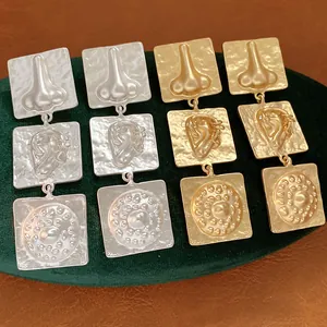 Detail of surrealist square drop earrings featuring embossed ear and nose motifs in metal finish.
