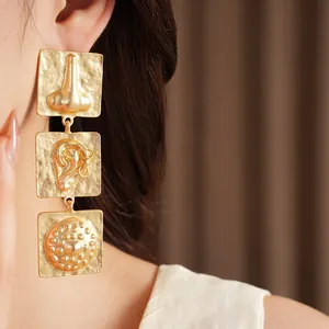 Close-up detail of surrealist gold square earrings with embossed body part motifs
