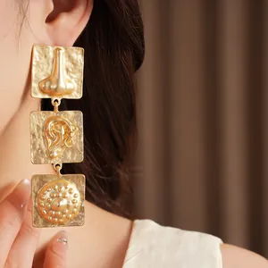 Close-up of oversized gold geometric earrings with abstract face motifs on a model.