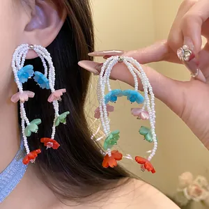 Close-up of colorful pearl flower drop earrings worn on ear and held by hand