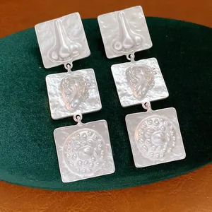 Close-up view of surrealist silver geometric square drop earrings with embossed face features
