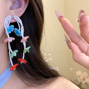 Macro detail of elegant colorful flower and pearl drop earrings worn by a model.