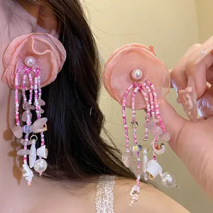 Macro view of pink fabric flower tassel earrings decorated with tiny shells and pink beads.