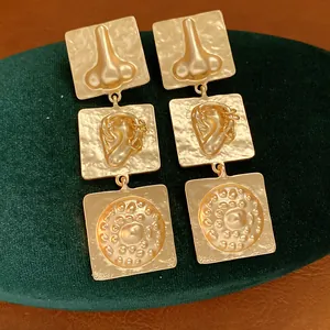 Exaggerated gold square earrings featuring unique surrealist nose and ear reliefs