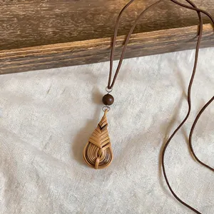 Detailed view of a hand-woven rattan waterdrop pendant on a brown leather cord necklace.