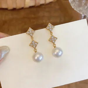 Detail view of elegant starburst zircon earrings with white pearls in 18K gold plating.