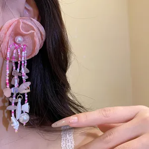 Close-up detail view of pink fabric flower tassel earrings with shell and bead accents