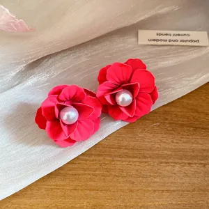Close-up of vibrant red painted flower stud earrings with a central pearl detail.