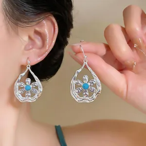 Detail view of elegant silver openwork teardrop earrings with a floral pattern and turquoise.