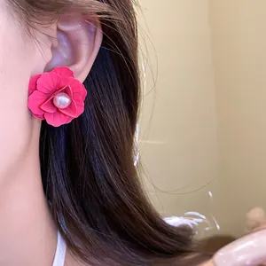 Close-up view of elegant pink painted flower earring with a pearl center worn on an ear