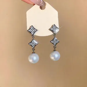 Close-up of starburst zircon earrings with elegant white pearl drops