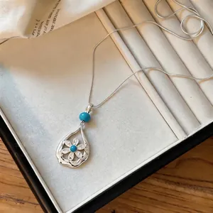 Detailed macro view of silver teardrop necklace with turquoise bead and flower design