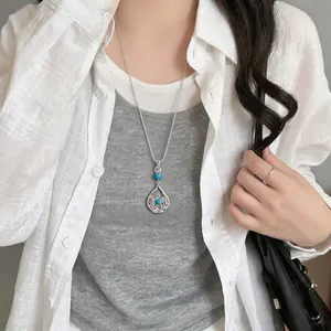 Elegant silver-toned necklace with a turquoise-beaded teardrop pendant on an Asian model