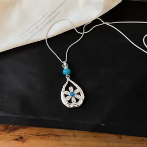 Detail view of silver hollow teardrop necklace with blue flower pendant