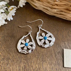 Close-up of silver-toned flower teardrop earrings with a blue turquoise center bead