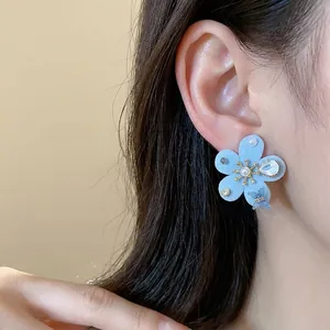 Elegante pendiente de flor azul flocado con perlas y circonitas puesto en la oreja