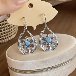 Close-up view of silver teardrop earrings featuring a blue flower center on velvet