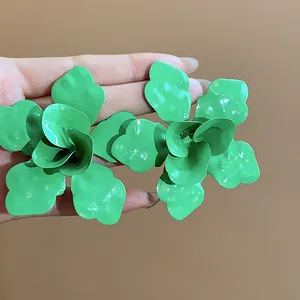 Detailed view of vibrant green oversized enamel flower stud earrings held in hand