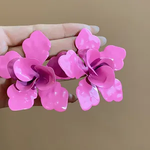 Close-up detail of oversized pink enamel flower earrings with a matte texture finish.
