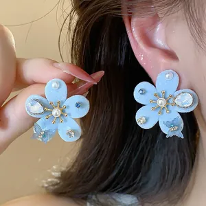 Primer plano de pendientes de flores flocadas azul claro con perlas y cristales de circón.