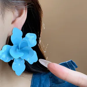 Detail of a large vibrant blue flower earring worn on an ear for visual scale.