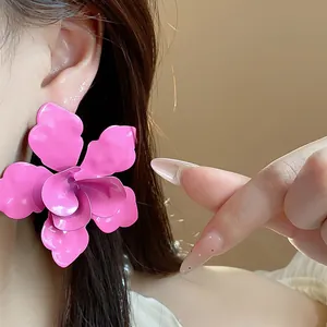 Detailed view of oversized fuchsia enamel flower stud earrings on an Asian model