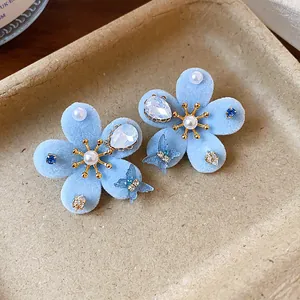 Primer plano de pendientes de flores de terciopelo azul con perlas y mariposas