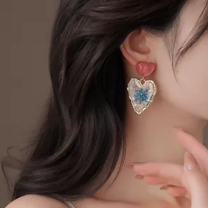 Close-up detail of a model wearing a transparent heart earring with dried blue flowers.