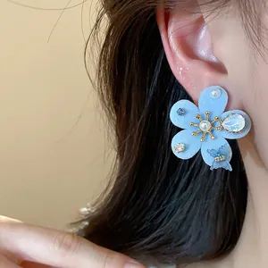 Vista detallada de un elegante pendiente de flor flocada azul claro con perlas y circonitas