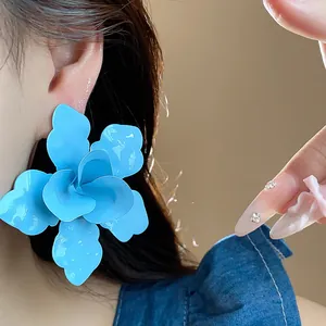Close-up of oversized light blue enamel flower stud earring worn by a model