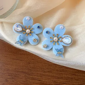 Primer plano de elegantes pendientes de flores de flocado azul con perlas y circonitas.