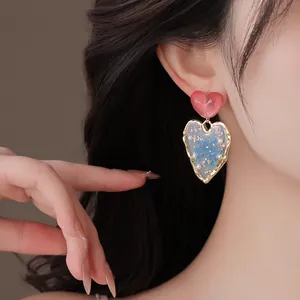 Close-up of elegant heart-shaped earrings with blue dried flowers and pearls on a model.