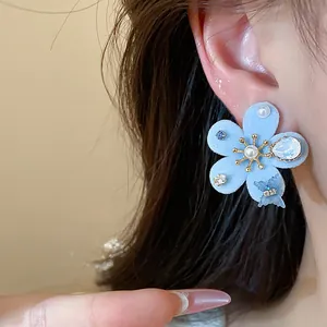 Elegante pendiente de flor flocada azul claro con perlas y circonitas brillantes puesto en la oreja
