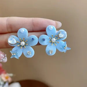 Detalle macro de pendientes de flores flocadas azules con perlas y acentos de mariposa de cristal