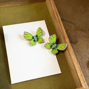 Detail view of vibrant neon green enamel butterfly stud earrings with rhinestones.