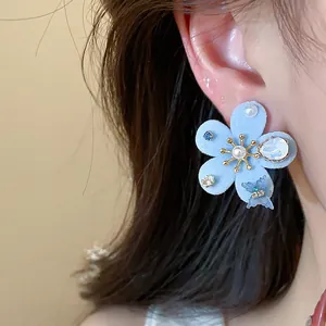 Primer plano de elegantes pendientes de flor azul flocada con una perla y circonita