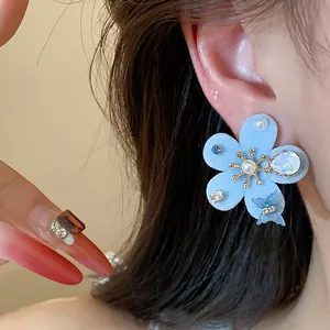 Vista detallada de un elegante pendiente de flor flocada azul con perlas y circonitas.